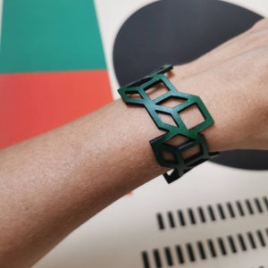 Peut inclure: Un bracelet en cuir vert avec un motif géométrique. Le bracelet est composé de formes découpées qui créent un motif de treillis.