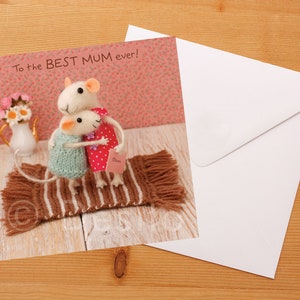 May include: A greeting card with a pink background featuring two white felt mice hugging on a brown and white striped rug. The card reads "To the BEST MUM ever!"