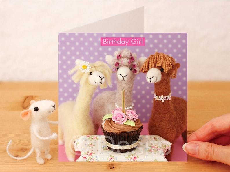 May include: A birthday card featuring three alpaca figurines with a cupcake and a single lit candle. The card has a purple background with white polka dots and the text "Birthday Girl!" in pink.