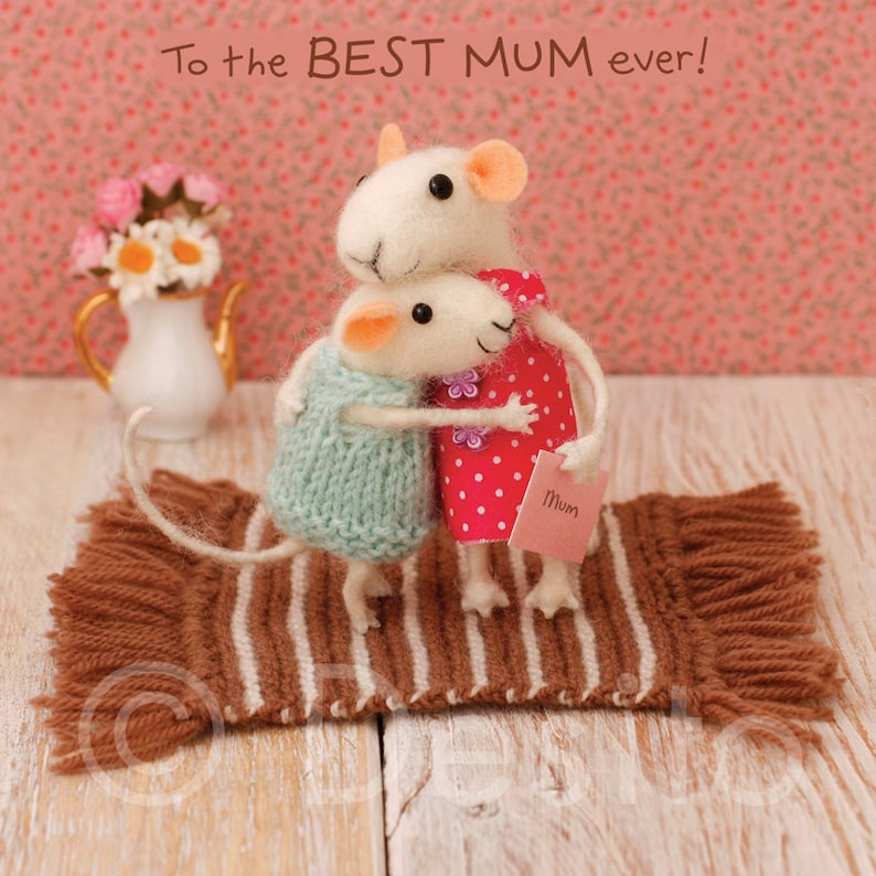 May include: Two white felt mice hugging on a brown and white striped rug. The mouse on the right is wearing a red and white polka dot dress and holding a pink card that says "Mum".
