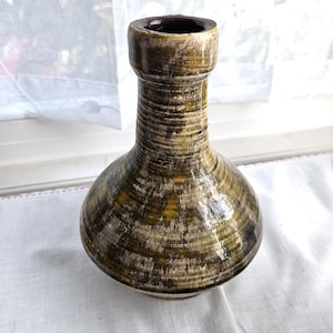 May include: A ceramic vase with a bulbous body and a cylindrical neck. The vase has a textured surface with a mix of brown, olive green, and cream colors. The opening is dark brown. The vase is likely for decorative purposes.