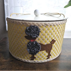 May include: A vintage yellow and white woven basket with a white lid and a decorative poodle applique. The poodle is brown with a black pom-pom style body and head, and a red collar. The basket has a braided trim.