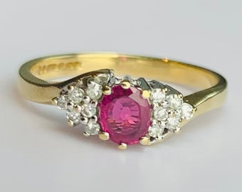 Pode incluir: Um anel de ouro com uma gema oval rosa cercada por gemas menores transparentes. O anel é inscrito com a palavra "HIGGS" na parte interna da banda.