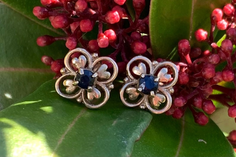 May include: A pair of silver earrings with a floral design and a dark blue gemstone in the center of each flower.