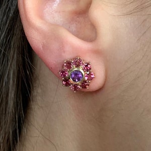 K&ouml;nnte beinhalten: Ein Paar goldene Ohrringe mit einem violetten Edelstein, umgeben von rosa Edelsteinen.