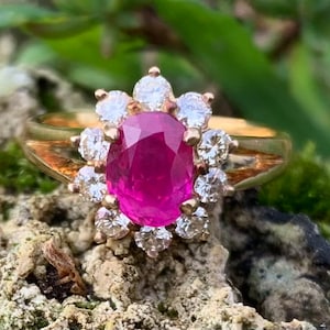 Può includere: Un anello d'oro con un grande rubino ovale circondato da un'aureola di diamanti più piccoli.