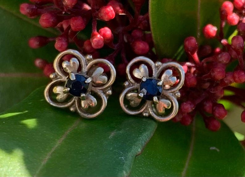 May include: A pair of silver earrings with a black stone in the center of each earring. The earrings are shaped like a four-leaf clover.