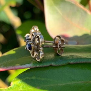 May include: A pair of silver earrings with a floral design and black gemstones. The earrings have a post back closure.