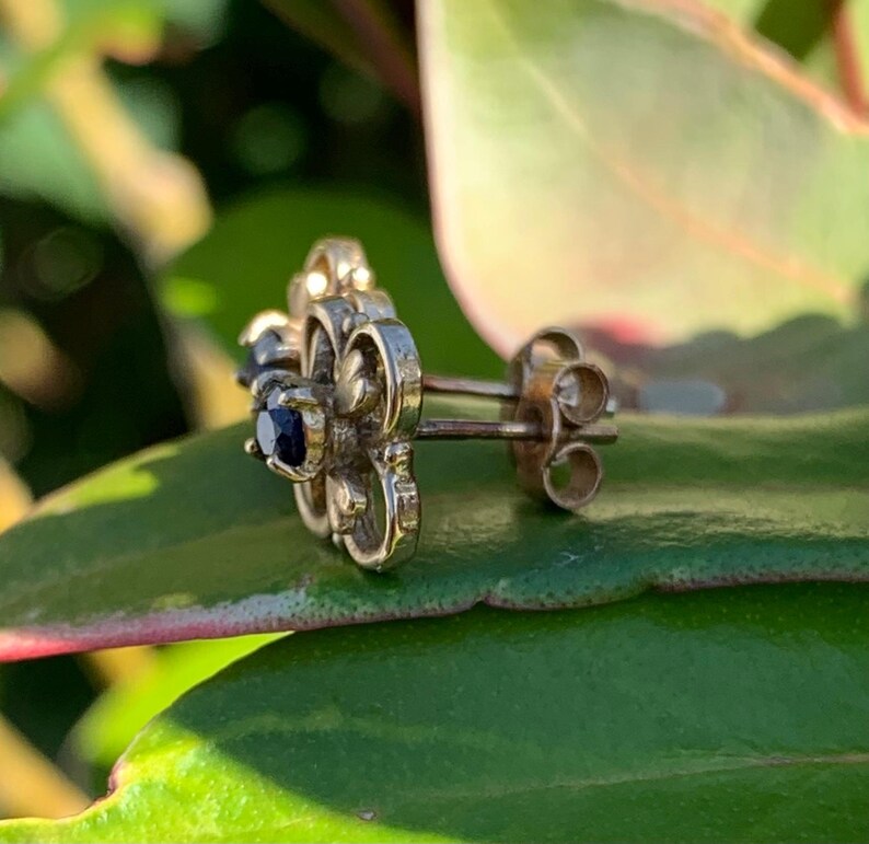 May include: A pair of silver earrings with a floral design and black gemstones. The earrings have a post back closure.