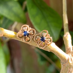 May include: A pair of gold earrings with a delicate floral design and a small blue sapphire in the center of each flower.