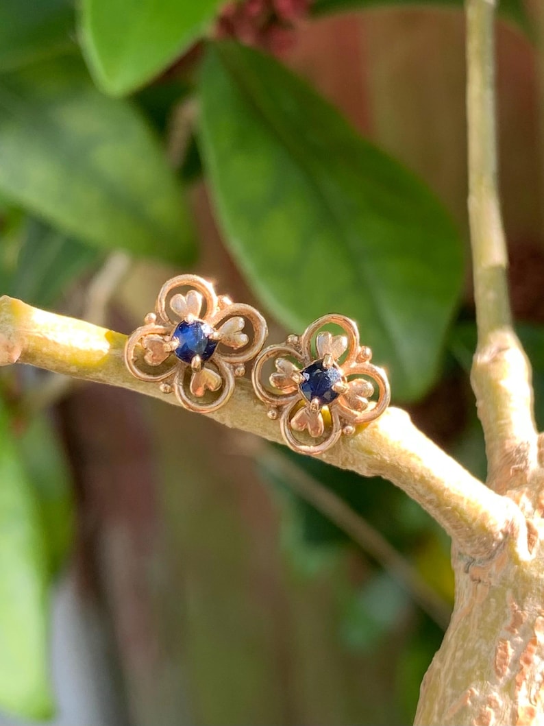 May include: A pair of gold earrings with a delicate floral design and a small blue sapphire in the center of each flower.