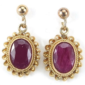 Peut inclure: Une paire de boucles d'oreilles en or avec des pierres précieuses en rubis. Les boucles d'oreilles ont un design détaillé avec une bordure en forme de corde et de petites perles autour du rubis.