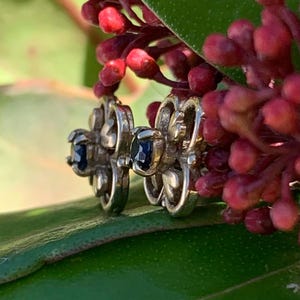 May include: A pair of silver earrings with a delicate floral design and dark blue gemstones.