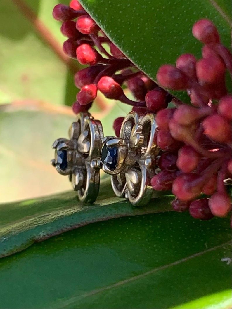 May include: A pair of silver earrings with a delicate floral design and dark blue gemstones.