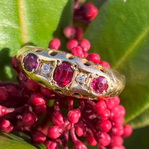 May include: A gold ring with a decorative design featuring four red gemstones and two smaller white gemstones.
