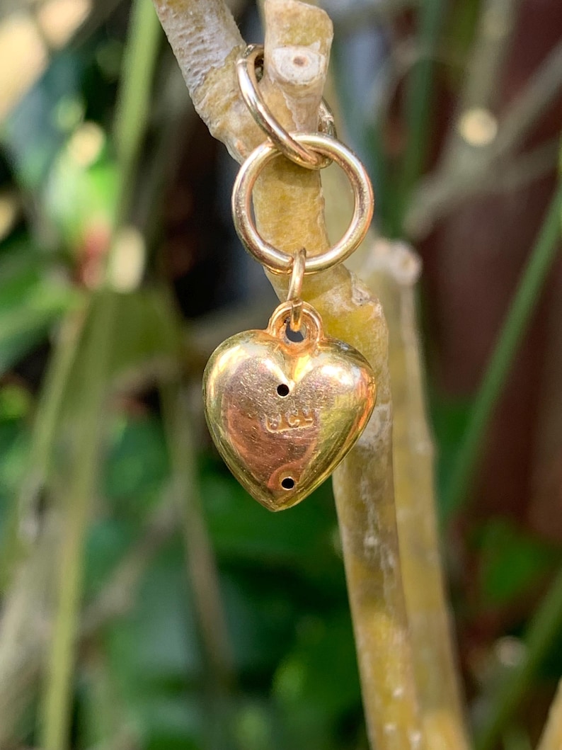 May include: A gold heart charm with a small loop at the top. The charm has a small inscription on the back that reads "925".