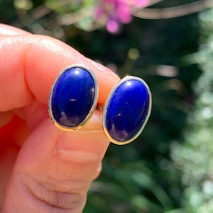 Könnte beinhalten: Ein Paar goldene Ohrringe mit ovalen Lapislazuli-Steinen. Die Steine sind tiefblau.