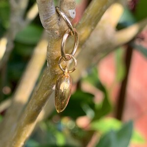 May include: A gold charm in the shape of a small, elongated heart, hanging from a gold jump ring.