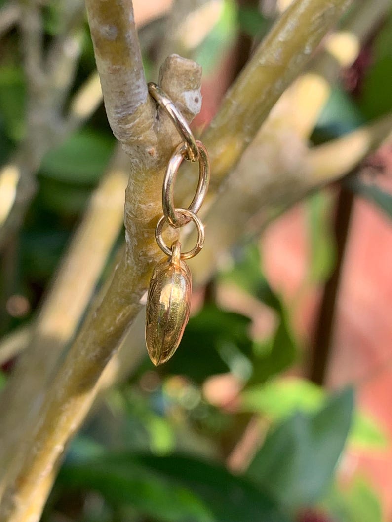 May include: A gold charm in the shape of a small, elongated heart, hanging from a gold jump ring.