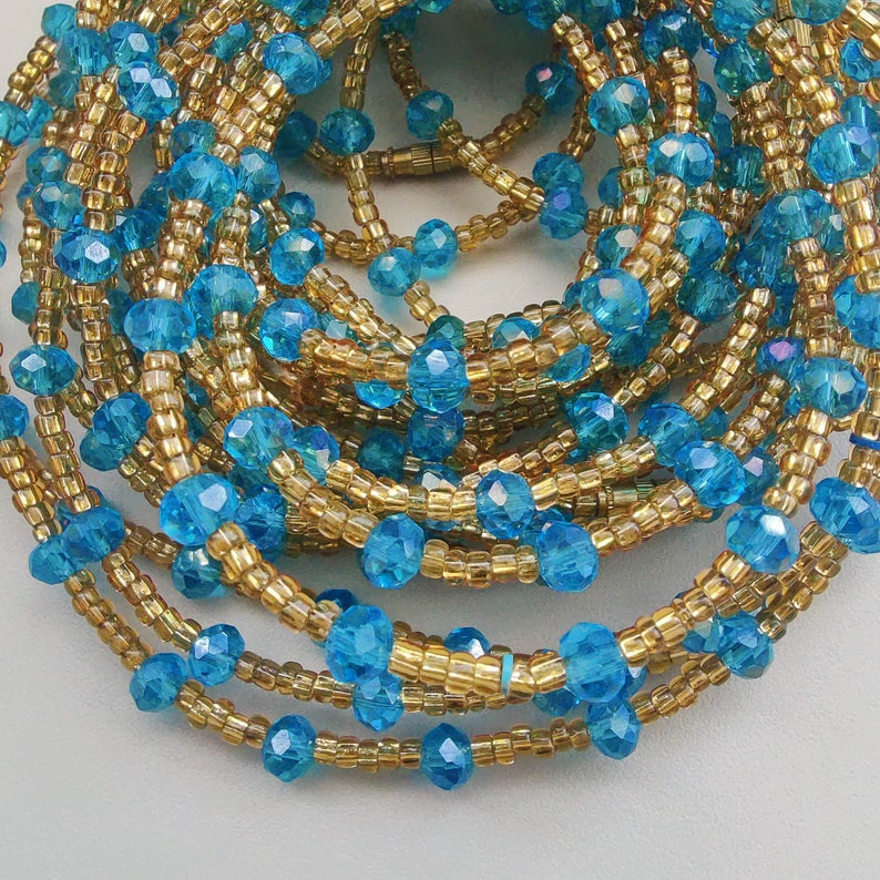May include: A close-up of a beaded waist chain with alternating blue and gold beads. The chain is made of small, faceted beads that create a shimmering effect.