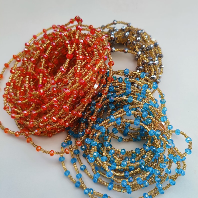 May include: Three strands of beaded jewelry in orange, blue, and silver. The orange strand is made of small, round beads with a gold sheen. The blue strand is made of small, round beads with a gold sheen. The silver strand is made of small, round beads with a silver sheen.