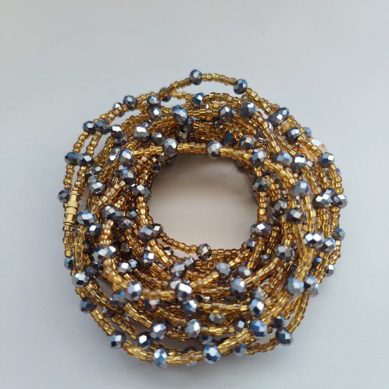 May include: A waist bead made of gold and silver beads. The beads are arranged in a circular pattern and are connected by a thin string. The beads are all different sizes and shapes.