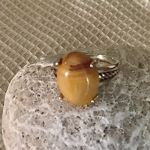 May include: A silver ring with a brown and white agate stone. The stone is oval shaped and has a natural pattern.