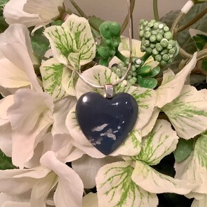 May include: A silver chain necklace with a dark blue heart-shaped pendant. The pendant has white and gray swirls throughout.