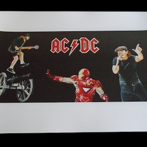 Puede incluir: Una impresión en blanco y negro de una banda de rock, AC/DC, con un logotipo de rayo rojo. La impresión presenta una caricatura de Angus Young, un guitarrista, de pie sobre un cañón, y una caricatura de Brian Johnson, el cantante principal, sosteniendo un micrófono. La impresión también presenta una caricatura de Iron Man, un superhéroe, con un traje rojo y dorado.