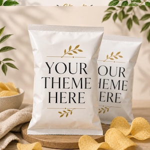 May include: Two white snack bags featuring the black text YOUR THEME HERE centered on the front. Each bag is decorated with gold leaf illustrations above and below the text. The bags are positioned upright on a wooden surface with potato chips.