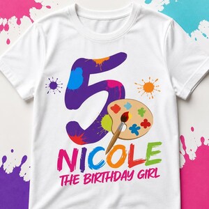 May include: White t-shirt with a colorful design for a fifth birthday. The design includes a large purple number 5 with paint splatters, a paint palette, and the text "Nicole The Birthday Girl" in bright colors.
