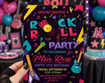 May include: A rectangular party invitation card with a black background featuring colorful rock and roll graphics including guitars, a microphone, and a vinyl record. The text reads: YOU'RE INVITED A ROCK ROLL PARTY TO CELEBRATE Mia Ross HAPPY 11TH BIRTHDAY.