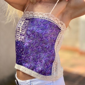 Puede incluir: Un top camisero patchwork con telas estampadas en tonos morados y blancos. Cuenta con finas tiras y encaje color crema en el escote y los bordes. El diseño combina texturas y patrones para un estilo único.