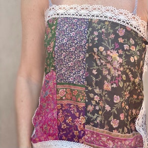 May include: A patchwork camisole with a white lace trim. The top features panels of fabric in various floral patterns and colors, including green, purple, pink, and black. The straps are thin and light blue.