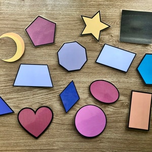 May include: A collection of colorful felt shapes, including a crescent moon, a star, a heart, a hexagon, a rectangle, a square, a pentagon, a diamond, a triangle, and a circle. The shapes are arranged on a wooden surface.