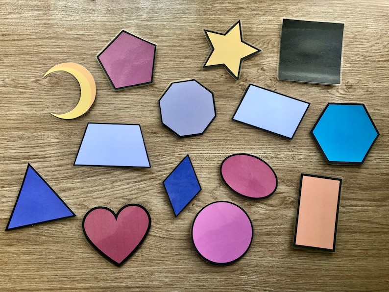May include: A collection of colorful felt shapes, including a crescent moon, a star, a heart, a hexagon, a rectangle, a square, a pentagon, a diamond, a triangle, and a circle. The shapes are arranged on a wooden surface.