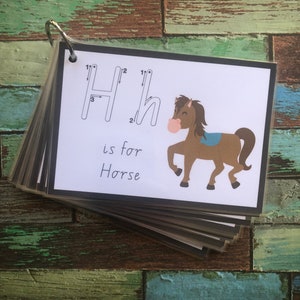 May include: A white card with a black border shows the letter H with tracing lines. The letter H is for Horse. A cartoon brown horse with a blue saddle is illustrated on the card.