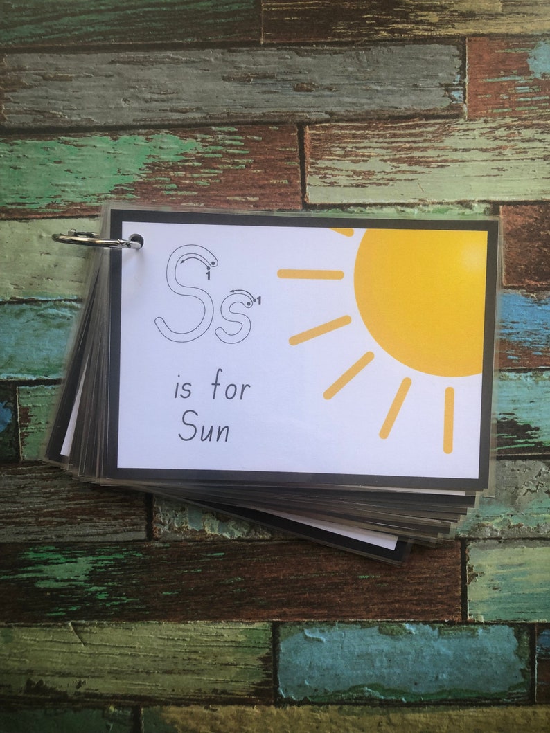 May include: A black and white flashcard with the letter "S" written in cursive and a yellow sun with rays. The text "S is for Sun" is written below the sun.