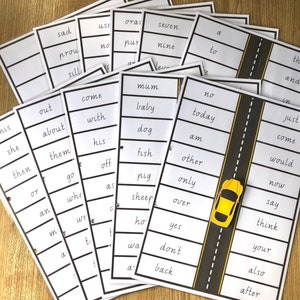 May include: A set of white flashcards with black text, displaying sight words. One card features a yellow car graphic on a road design. The cards are arranged on a wooden surface, suitable for educational use.