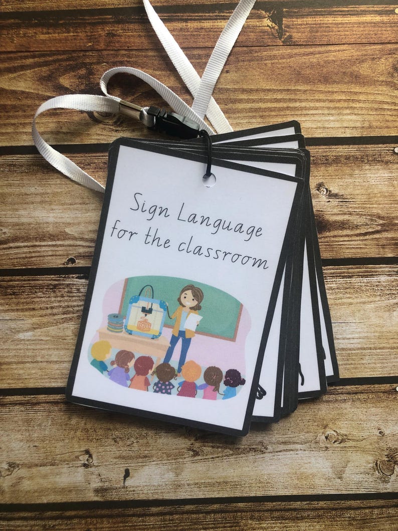 May include: A set of flashcards with black borders and a white background. The cards feature illustrations of a teacher and students in a classroom setting. The text on the front card reads "Sign Language for the classroom".
