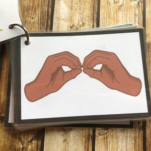 May include: A close-up of a sign language hand gesture. The hands are shown in a brown skin tone, with the fingers forming a circle shape. The background is white.
