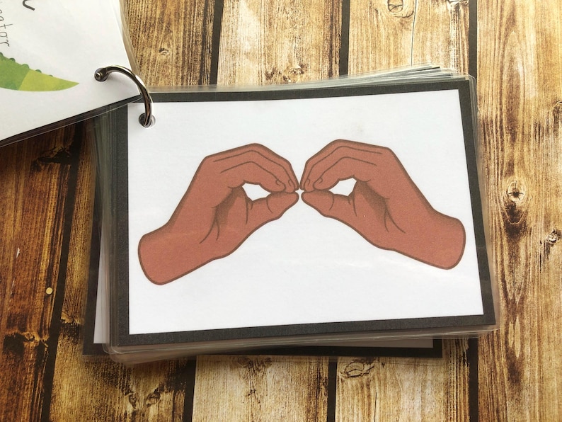 May include: A close-up of a sign language hand gesture. The hands are shown in a brown skin tone, with the fingers forming a circle shape. The background is white.