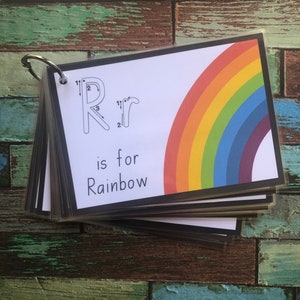 May include: A colourful rainbow with a black border is on a white card with the letter "R" and the words "is for Rainbow".