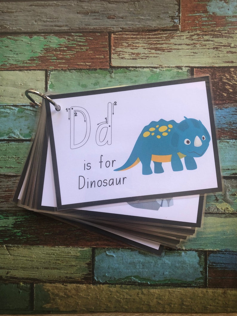 May include: A printable flashcard featuring a blue and yellow dinosaur illustration. The card shows the letter "D" with dotted lines to help trace the letter. The text "D is for Dinosaur" is printed below the illustration.