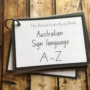 May include: A black binder with a white cover and a silver ring binder. The cover has the text "The Bored Kids Busy Book" and "Australian Sign Language A-Z".