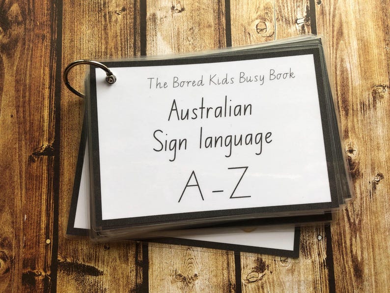May include: A black binder with a white cover and a silver ring binder. The cover has the text "The Bored Kids Busy Book" and "Australian Sign Language A-Z".