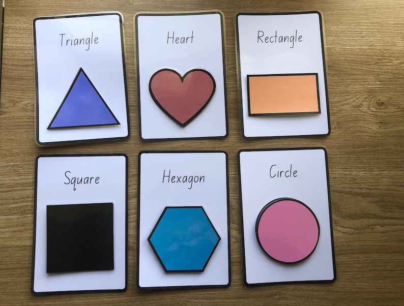 May include: Six white cards with black borders, each featuring a different shape: triangle, heart, rectangle, square, hexagon, and circle. The shapes are filled with different colors: blue, red, orange, black, blue, and pink.