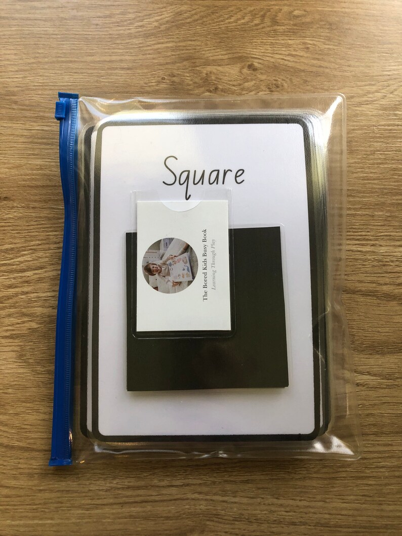 May include: A white plastic bag with a zipper closure contains a white card with the word "Square" written in black. The card is attached to a black square piece of paper. The card also has a smaller card attached to it with the text "The Bored Kids Busy Book Learning Through Play".