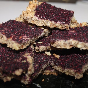 May include: A stack of homemade granola bars with a purple berry filling and a crunchy oat topping.