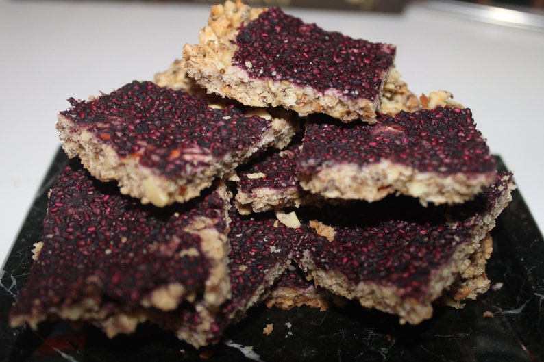 May include: A stack of homemade granola bars with a purple berry filling and a crunchy oat topping.